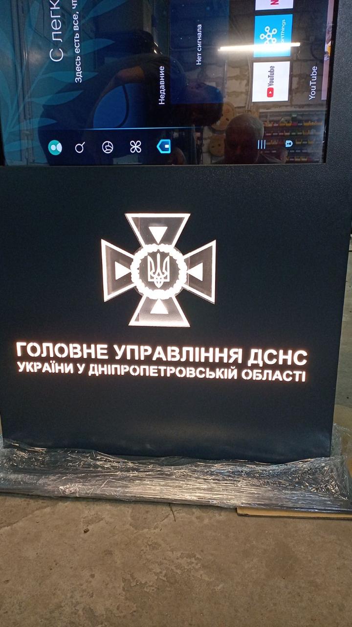 Close-up of the illuminated DSNS Dnipropetrovsk regional emblem and lettering on the lower body of the QS55 touch kiosk