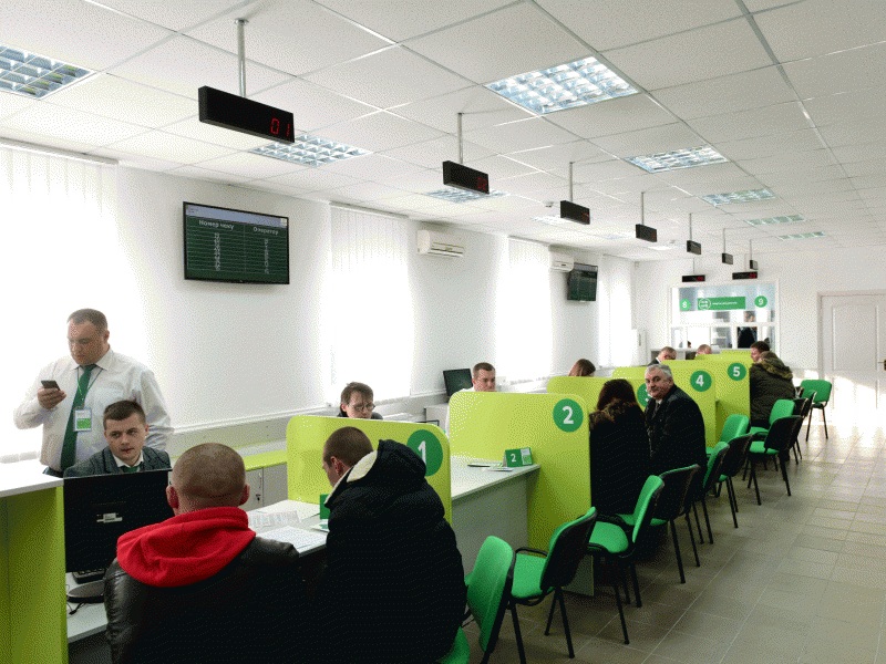 MIA Service Center hall with overhead LED queue displays and visitors